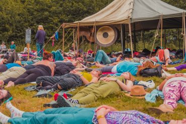 People lay next to each other with their eyes closed, a set a gongs are in the middle fo them.