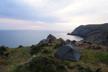 A tent sits on the edge of a coastal path, the sea is in the distance.