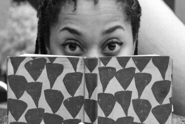 A person is looking at the camera with a book covering the bottom half of their face.