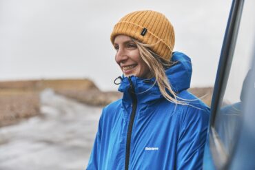A woman stands next to a vehicle in a waterproof jacket and yellow hat.